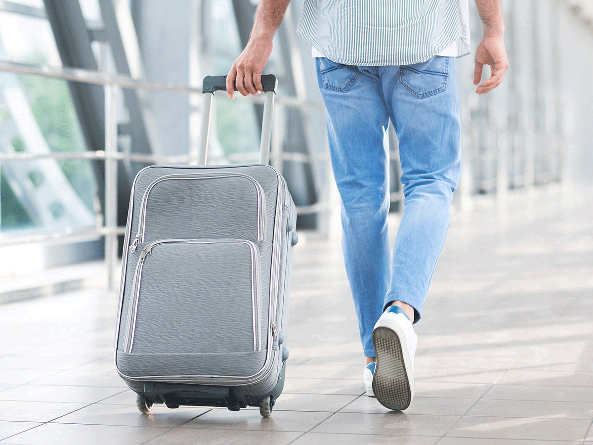 Male traveler walking through an airport pulling a rolling bag